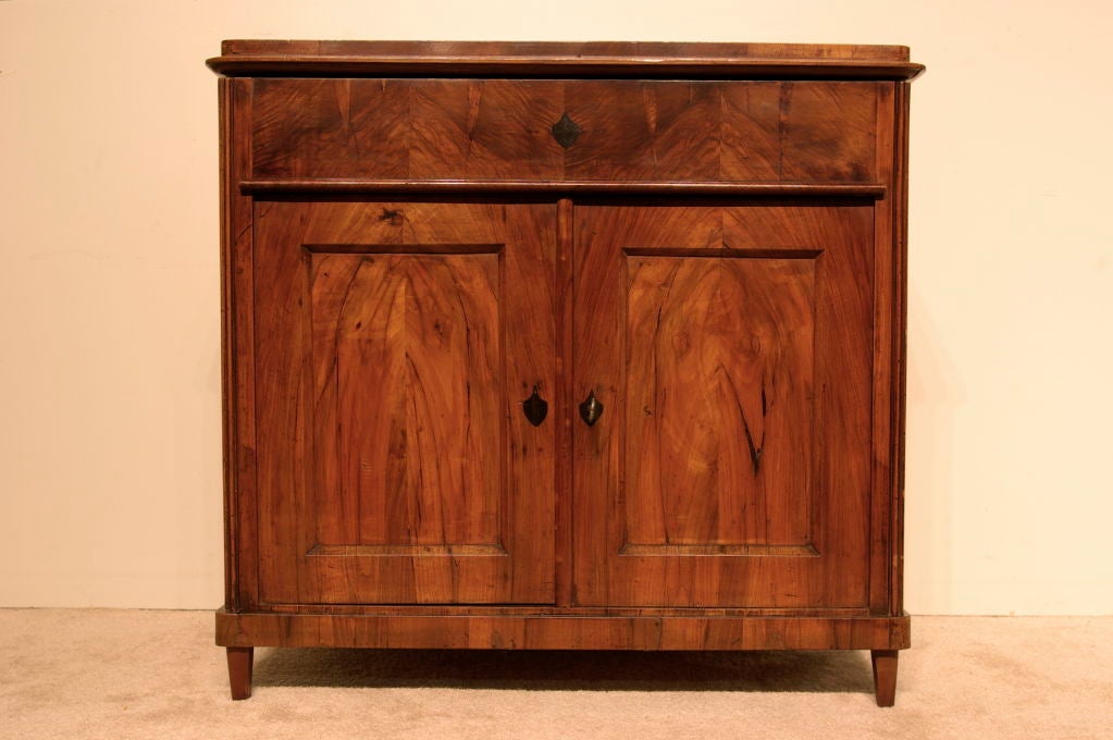 A stunning Biedermeier buffet in walnut.  This rare buffet features a hinged top that reveals a shallow storage area, perfect for an occasional bar.  The main storage area retains its original shelf and working lock. Excellent veneer choices and