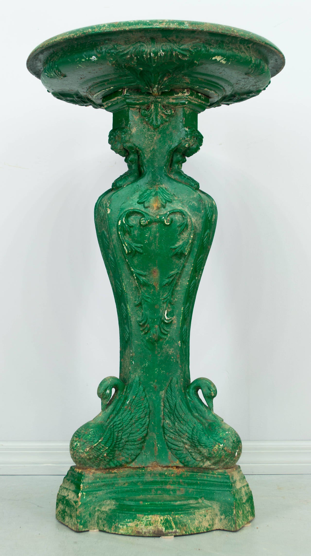 19th century French cast iron bird bath with old green painted patina. In two pieces with basin resting on pedestal. A trio of swans decorates the base. Total weight is 200 lbs. 
More photos available upon request. Please visit our showroom in