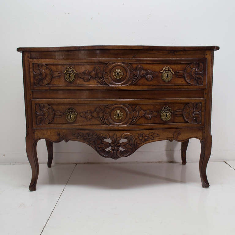 A superb serpentine front walnut commode from the Burgundy Province, with two dovetailed drawers retaining its original brass hardware, with fine carvings and a pierced apron. Top is constructed of two planks and the chest retains a beautiful rich