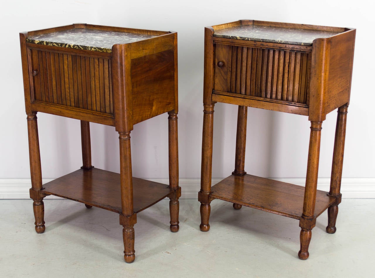 Pair of similar 19th century Louis Philippe side tables or night stands made of solid walnut, each with a tambour door and grey marble top. Almost identical, with only slightly different proportions. Waxed patina. 
Dimensions of table on the left: