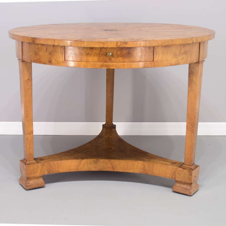 A center table of veneer of elm wood on pine wood with a long dovetailed drawer and three tapered legs. The table has some wooden wheels on the bottom. Beautiful workmanship on the top and retaining a French Polish finish. The height from the bottom