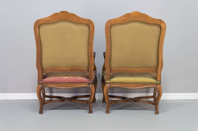 A pair of large French fauteuils with original petit-point tapestry. Hand carved walnut frames are sturdy with comfortable seating. Upholstery is in good condition, with one armchair having a light pink color and the other pale green. Please refer