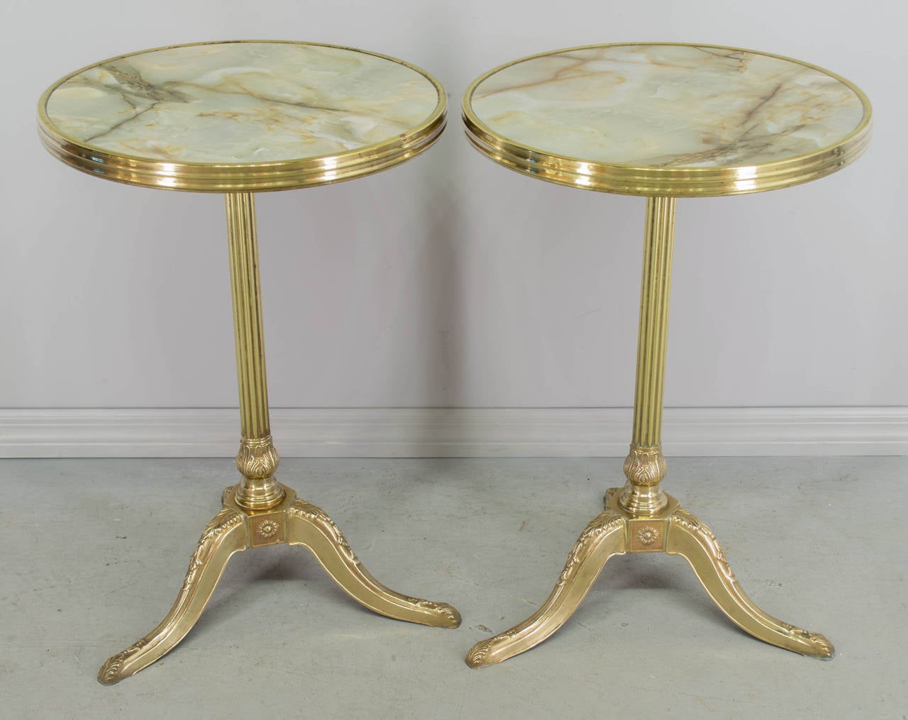 Pair of French bistro tables from a Paris cafe. Each table with a solid polished cast brass base and faux marble Formica top. Unusual that these tables are made of brass, as cast iron was more common. As always, more photos available upon request.