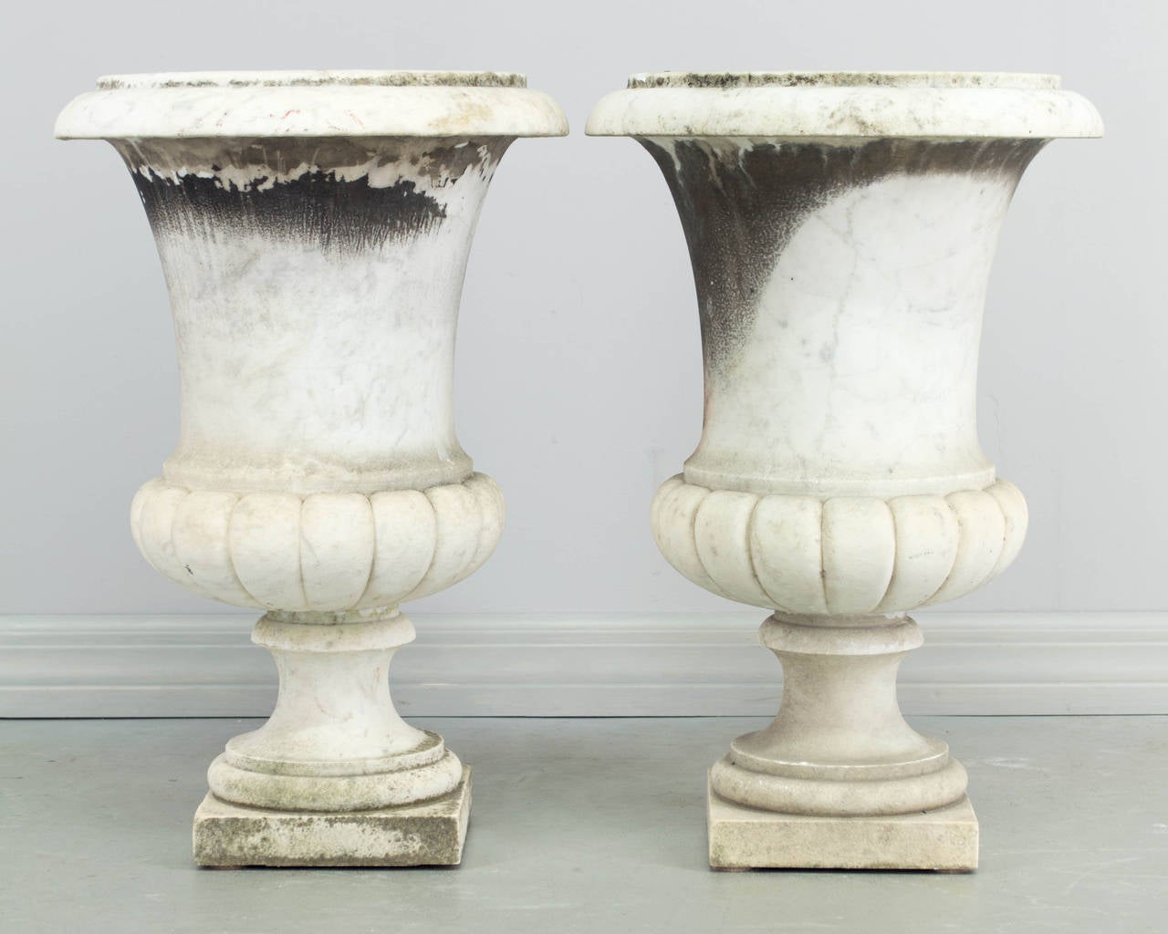 Pair of 19th century French urns, made of white marble with grey veining and retaining old weathered surface. In two parts, the planters rest on the pedestal base. The base of the pedestal is is 6.75