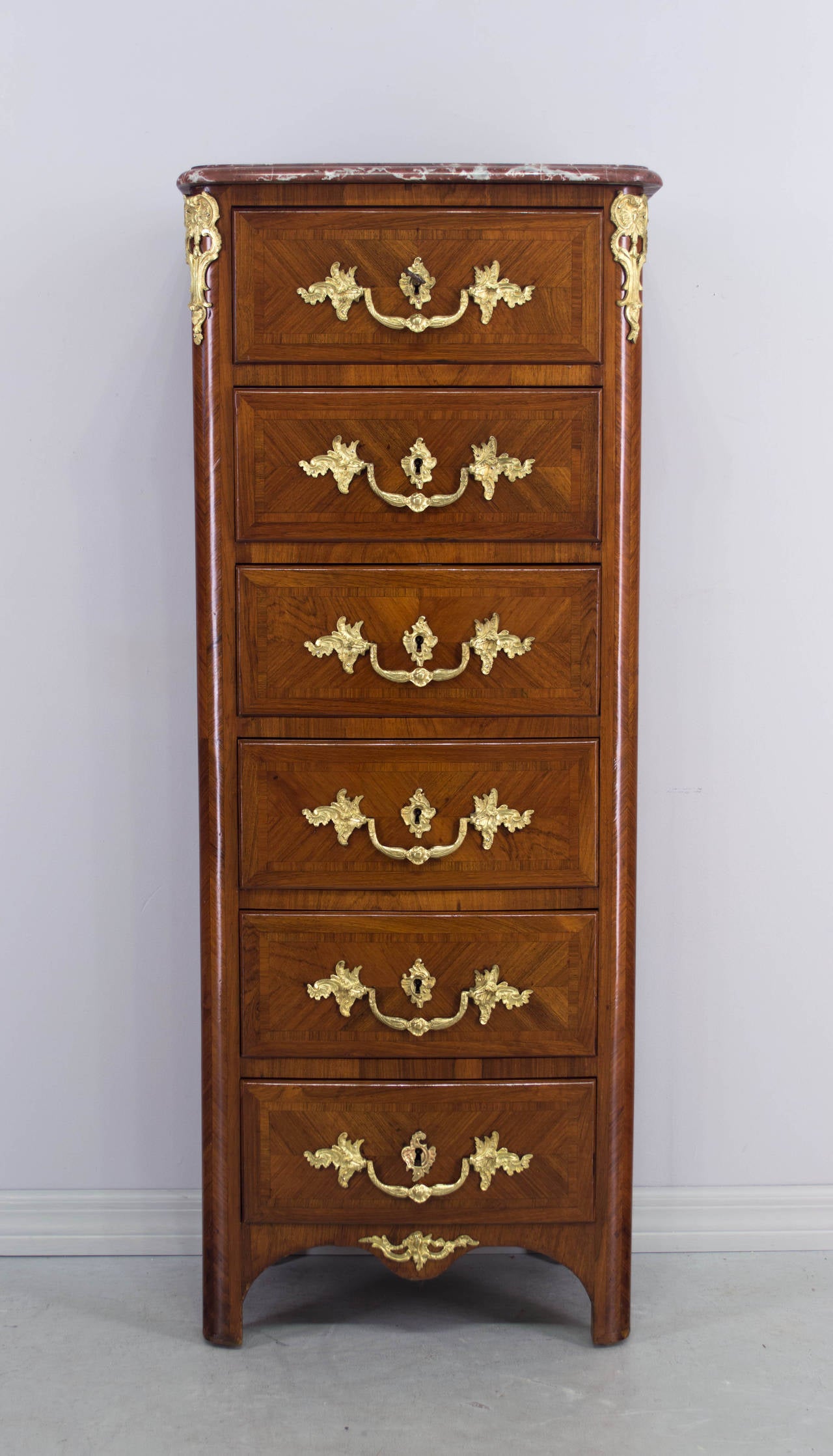 French Regency style tall chest or chiffonier with inlaid veneers of mahogany and tulipwood with oak as a secondary wood. Six dovetailed drawers with original bronze doré hardware. One key for all locks. Rouge royal marble top. French polish