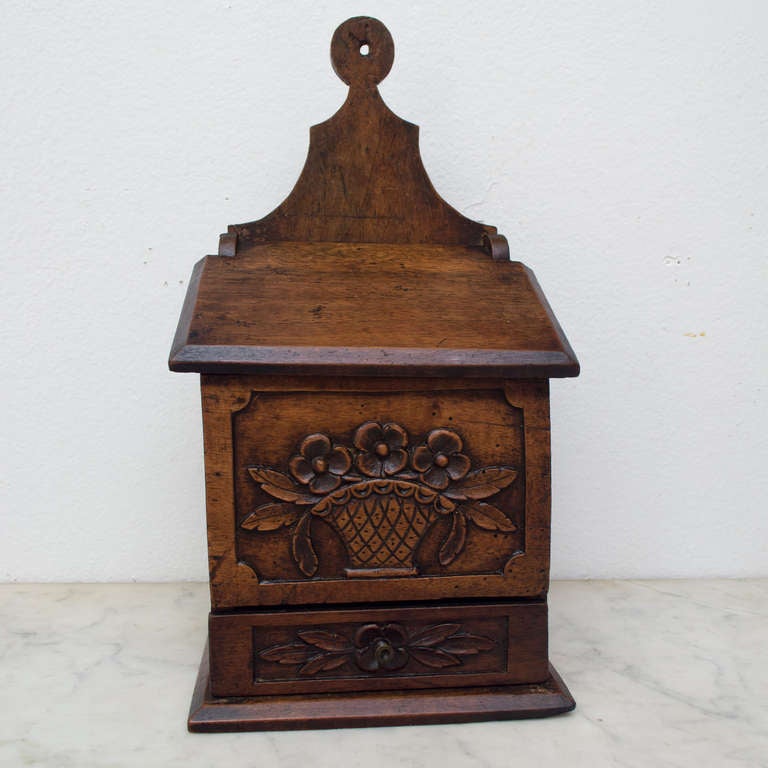 Made of walnut, a Provencal salt and pepper box with a carved flower basket above a drawer.