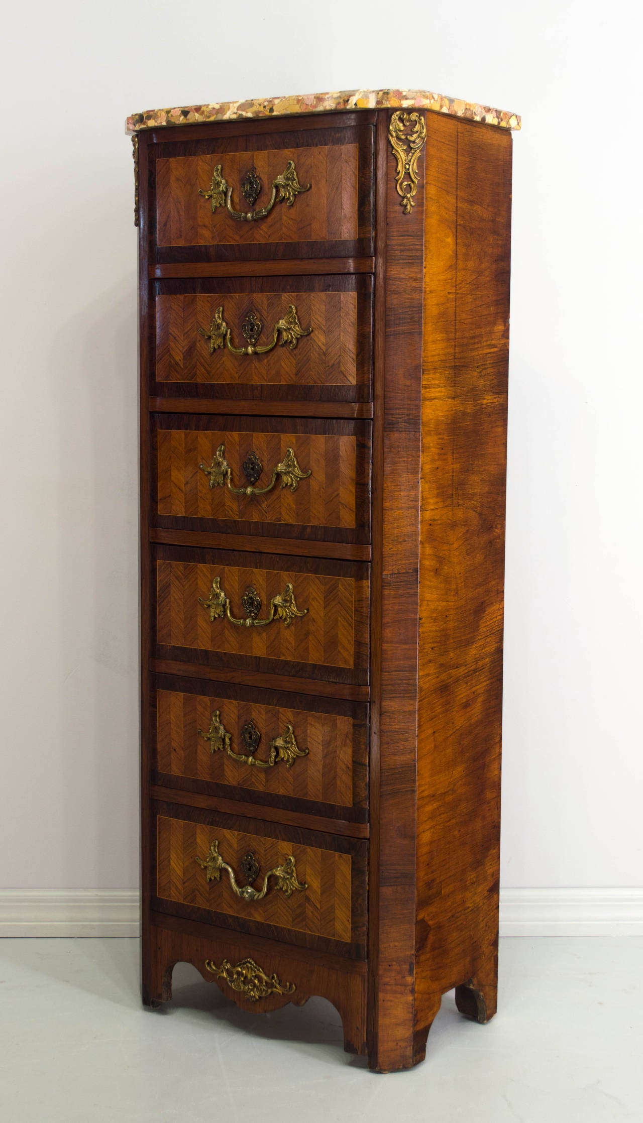 A tall chest with six dovetailed drawers, inlaid with of veneers of mahogany, walnut and rosewood. Bronze hardware. Note: The top and bottom drawer pulls do not match the others. Locks are present, but there are not keys. Marble top. French polish