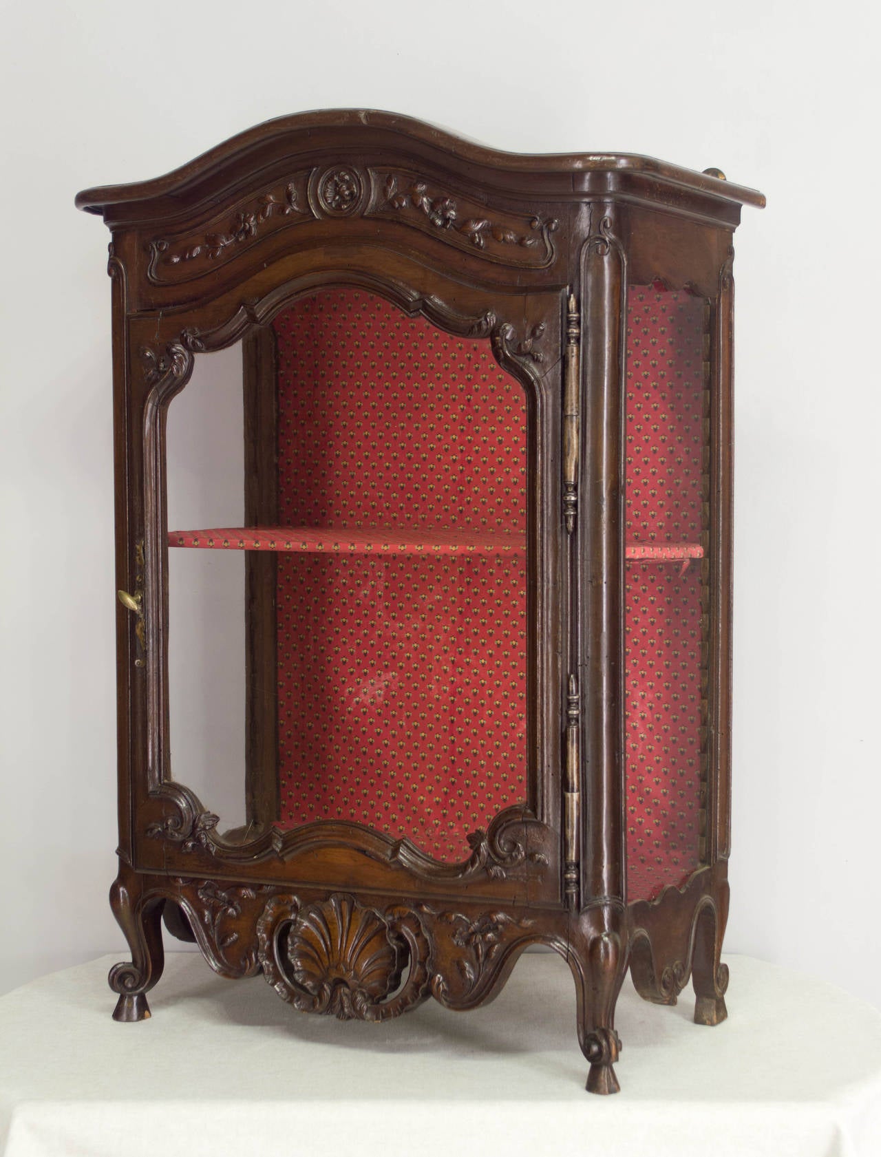 A 19th century Louis XV style verrio from Provence made of walnut with glass door and sides. Fine hand-carved details with a pierced apron and a small chapeau de gendarme crown. Interior has one shelf and is lined with fabric. A verrio is a small