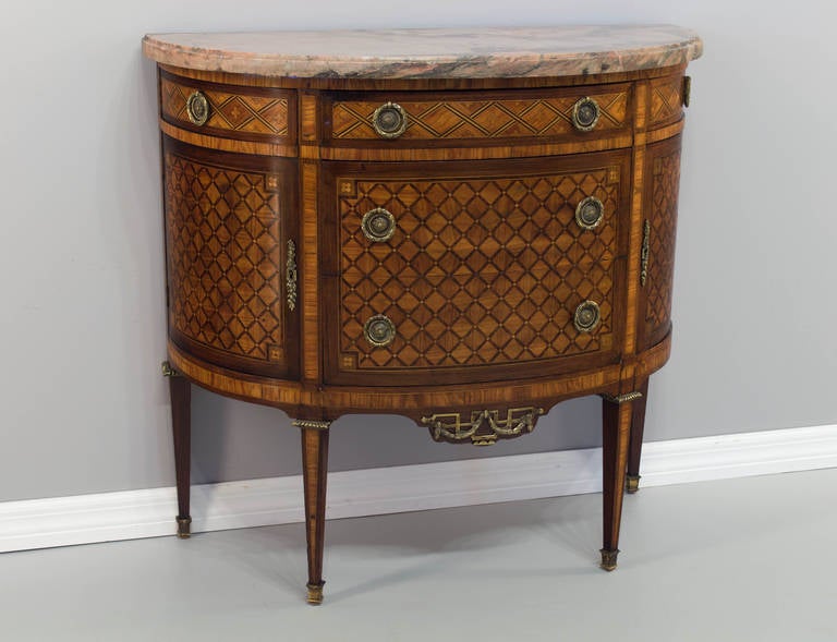 A fine marquetry commode in the shape of a half moon having seven openings, (five drawers and two doors). Walnut, mahogany and tulip wood veneer, original bronze hardware and marble top. As always more photos are available upon request and we have