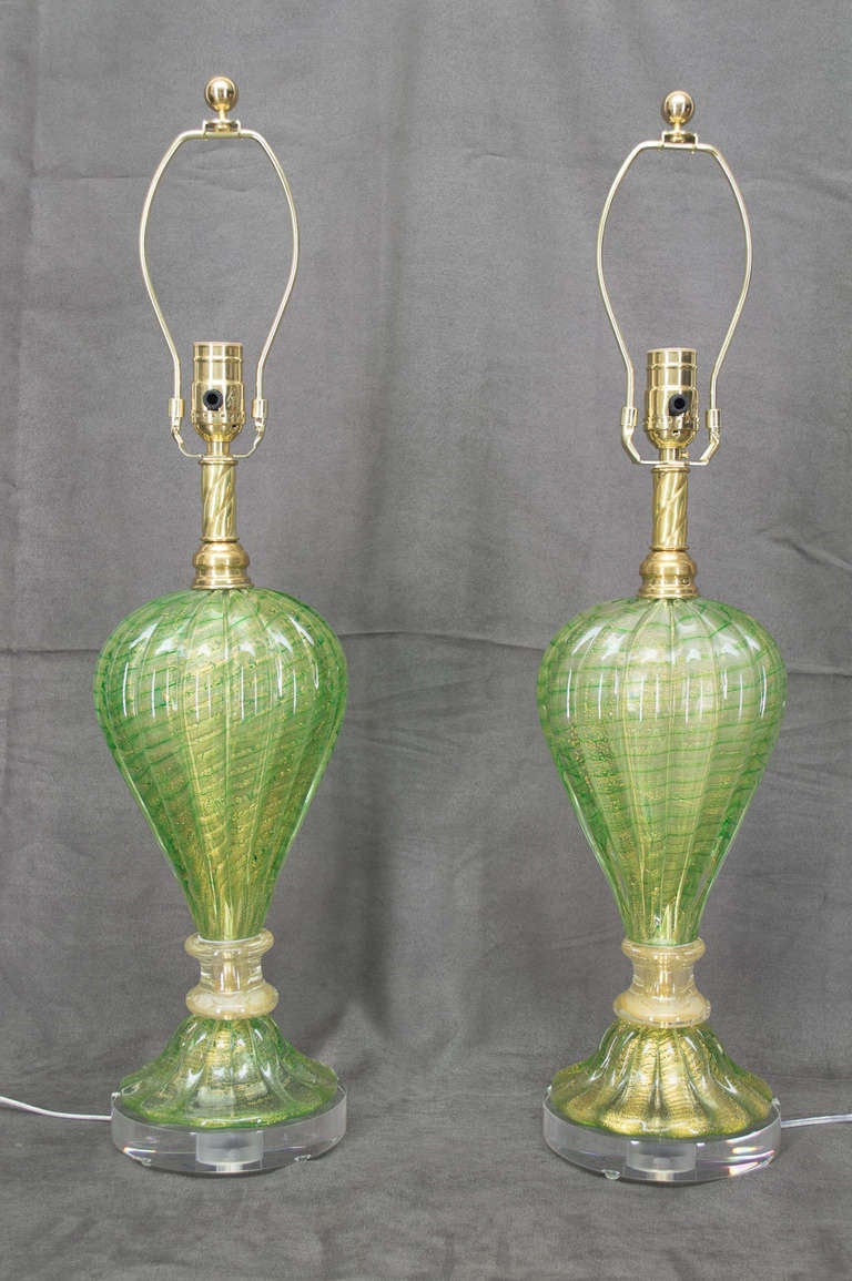 Pair of Murano glass lamps in beautiful shade of apple green with gold inclusions. Original polished brass neck and collar. Rewired, new sockets and clear lucite base. White linen drum shades are 14