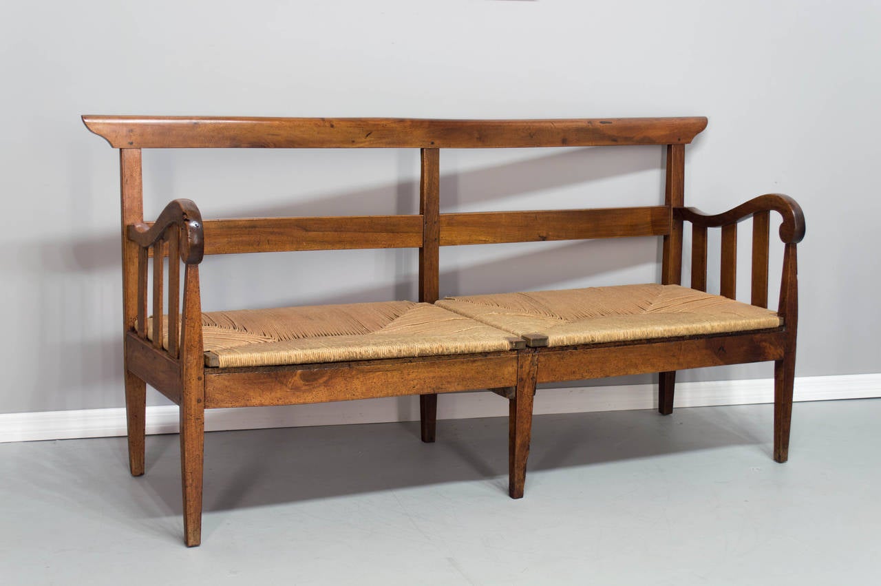 An 18th century solid walnut bench with six tapered legs and rush seat. Excellent construction on this banquette, all pegged and mortise, sturdy with a nice large seat. The rush seats are old but not original and it was probably covered with fabric