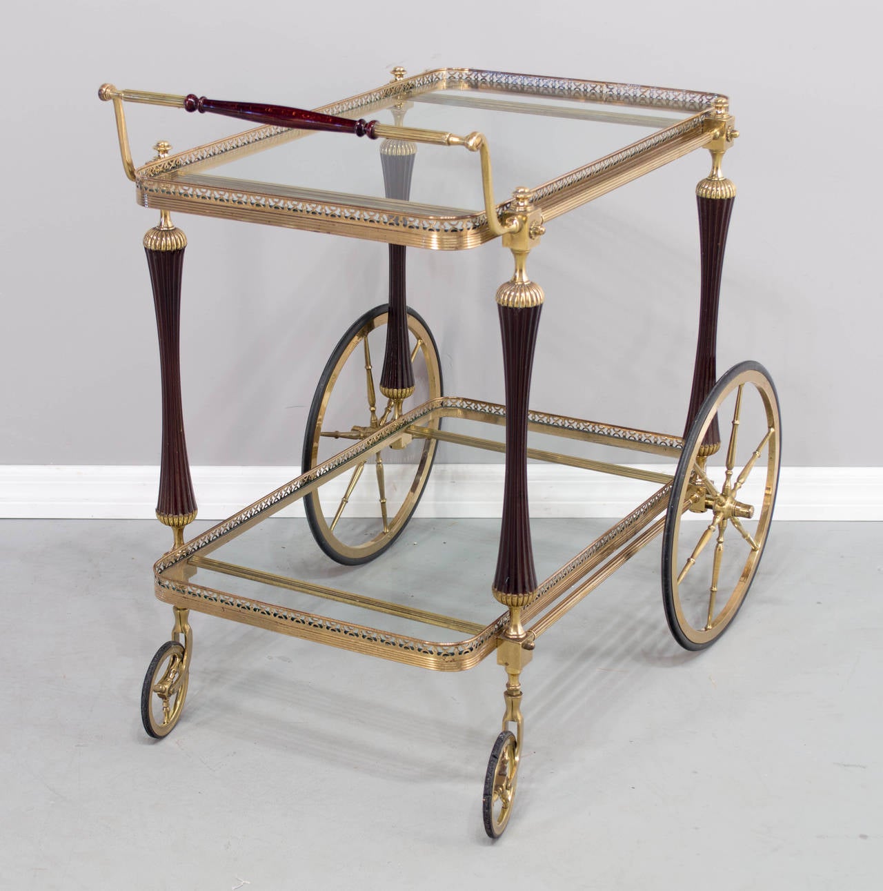 A French solid brass and mahogany bar cart. The brass is polished but not lacquered and the glass shelves are new. The rubber of the front right wheel is a little worn but the cart rolls well.
The glass shelves are 16.5
