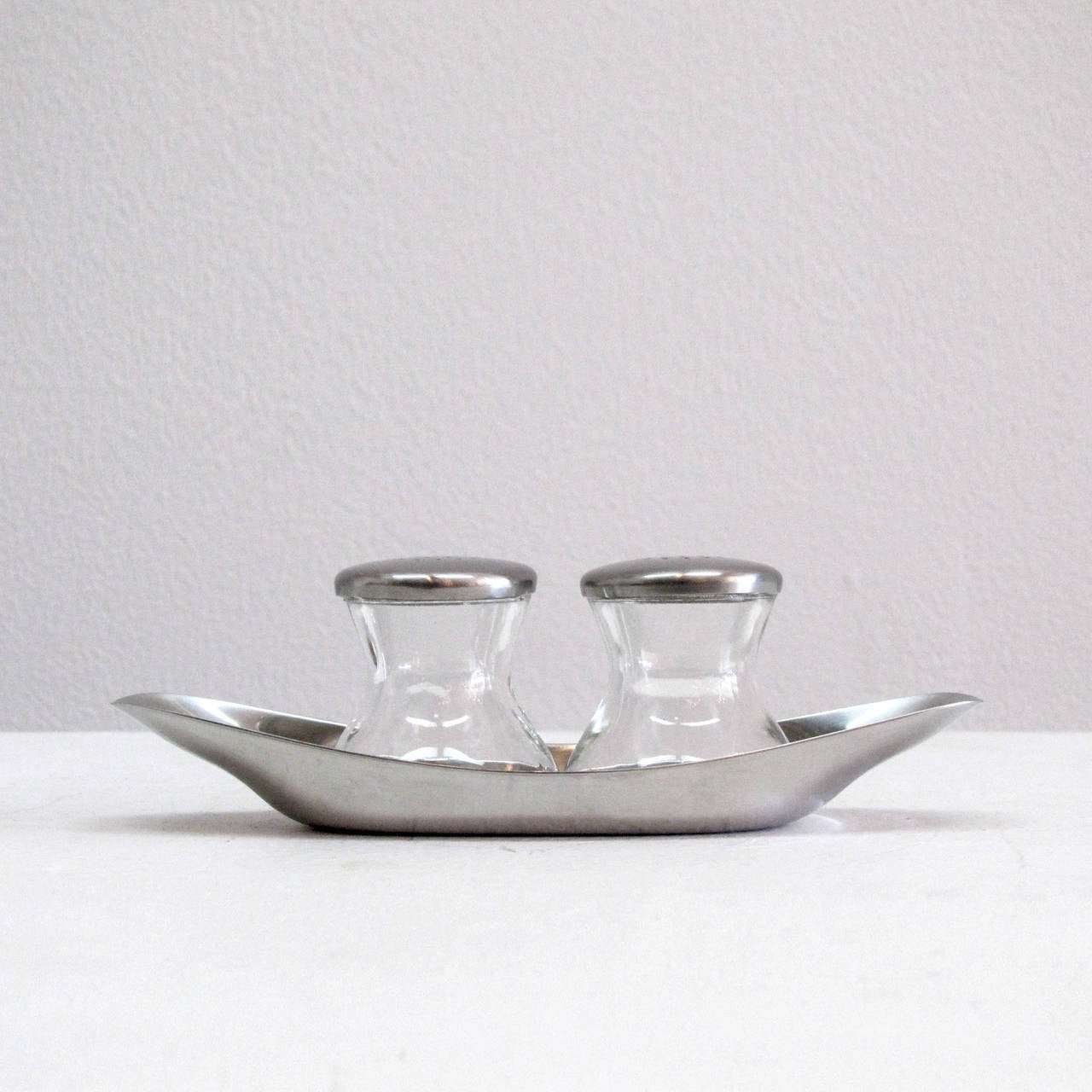 classic, complete salt and pepper shaker set by Wilhelm Wagenfeld for WMF, WV 505. the set includes two pressed glass shakers with perforated lids and a cromargan (stainless steel derivative) plate/holder, part of the MoMA permanent collection