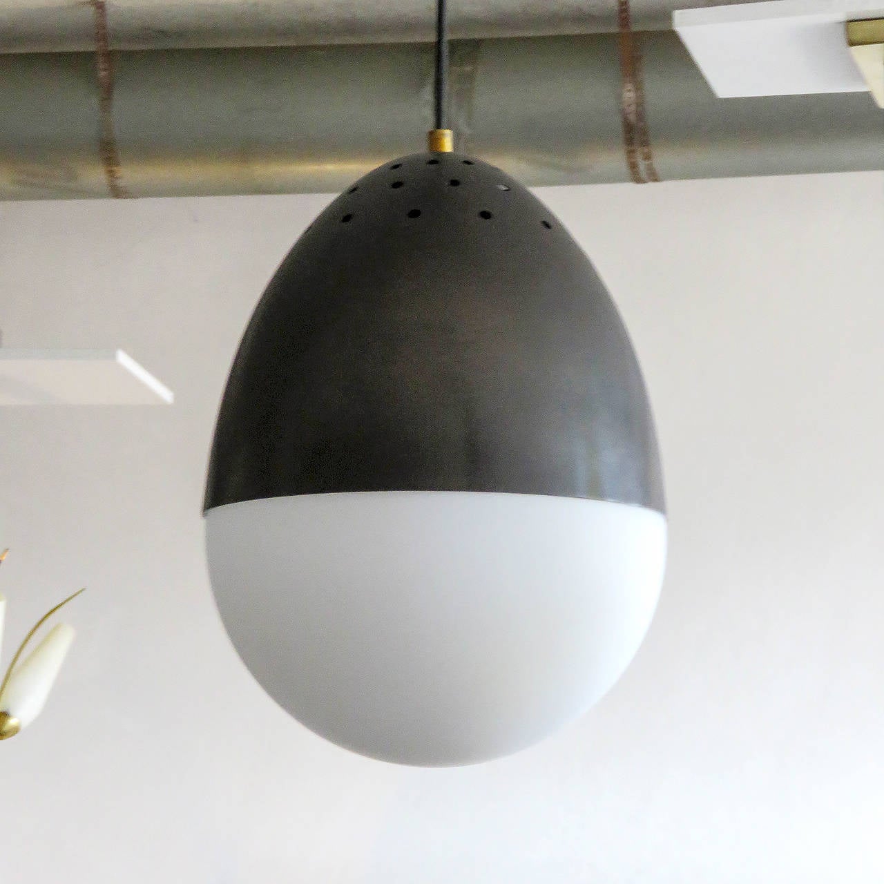 Elegant Italian milk glass pendant light by Stilnovo, matte milkglass globe with dark brass patinated, partially perforated hood, suspended from black cloth wire.