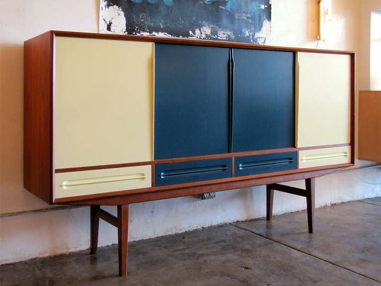 unique high teak sideboard with four sliding front doors and four drawers painted two tone by Pernille Albers, tapered legs with stretchers, inside with several shelves, cutlery drawers and a bar compartment with mirrored/pattered glass