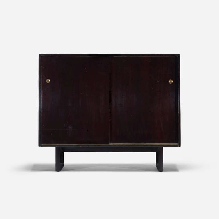 Cabinet features two sliding doors concealing eleven drawers and one pull-out hanging tie storage. Signed with decal manufacturer's label to drawer: [Modern Original Widdicomb].