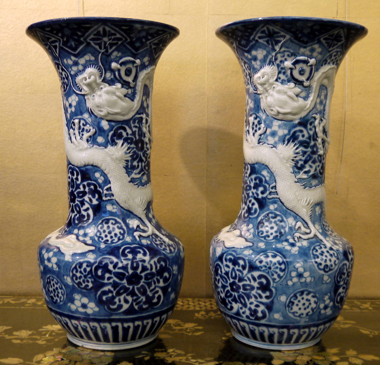 A very dramatic and decorative pair of Japanese antique vases with floral background, and raised design of fierce dragons encircling each vase.