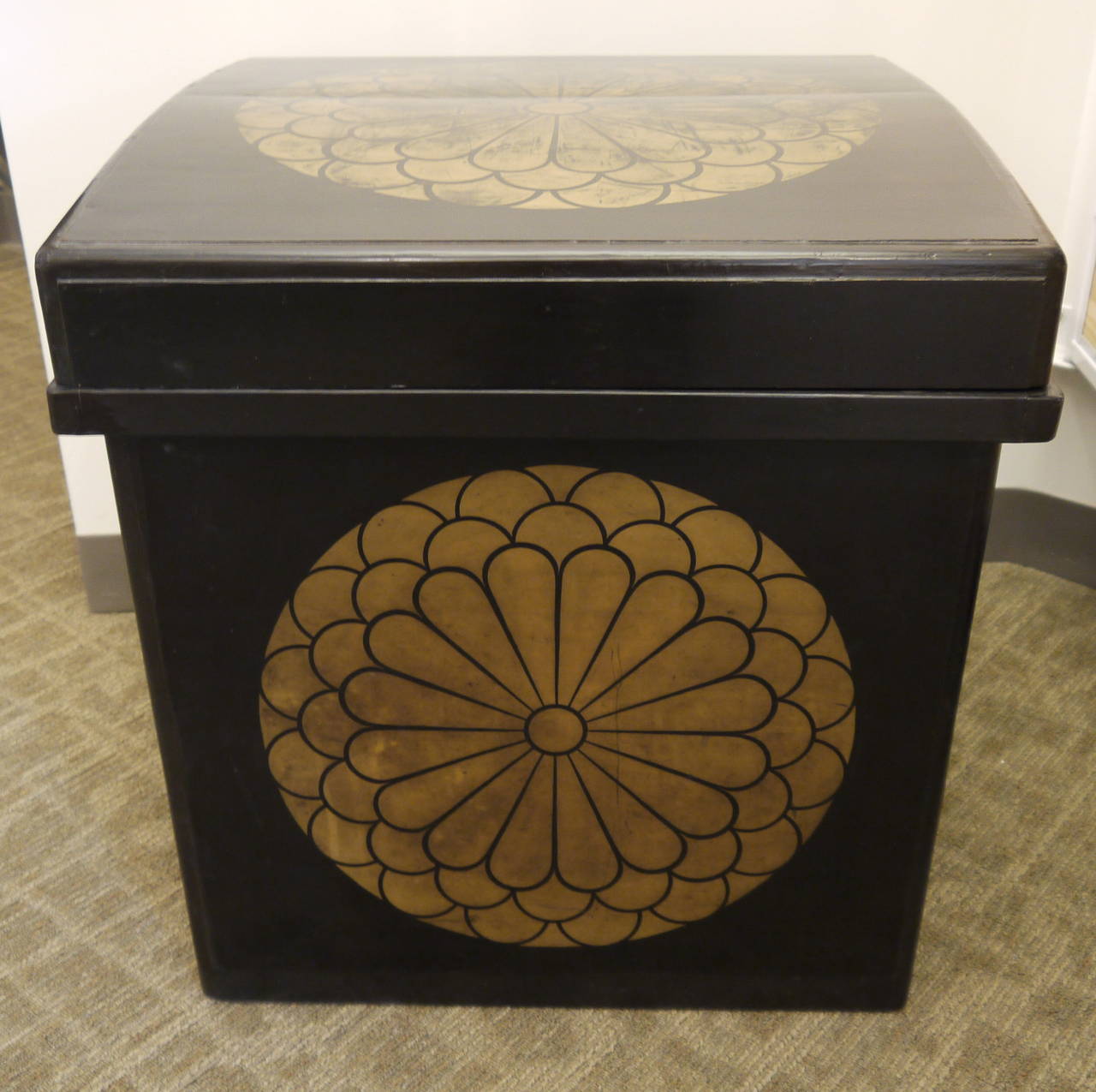 A large black lacquer Japanese antique storage box with lid.

There is a large, bold gold family crest on the top and two sides.

Lid has a slightly curved shape.