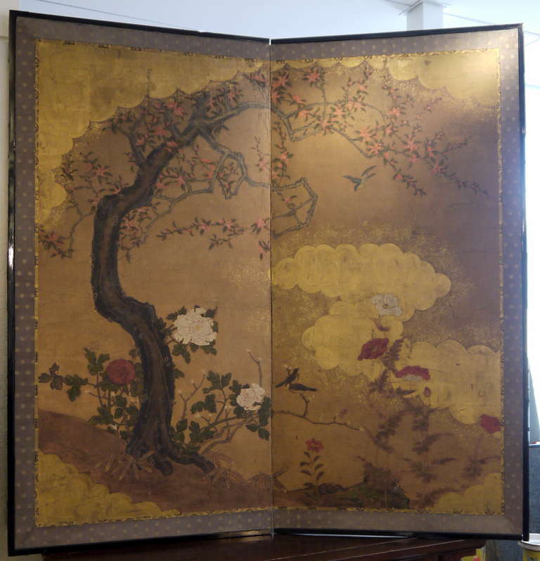 A beautiful large scale two-panel Japanese screen with hand painted design of flowering tree, peonies, and birds, with scattered gold leaf clouds.

This screen is framed in the traditional manner, with brocade borders, a black lacquer frame, and a