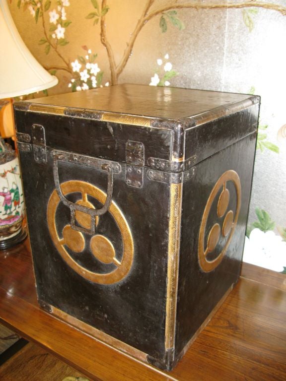 A 19th century Japanese armor storage box.<br />
<br />
Wood, covered in black leather, with design of gold family crests on three sides, and a kanji symbol on the fourth side.<br />
<br />
With lid, and hardware.