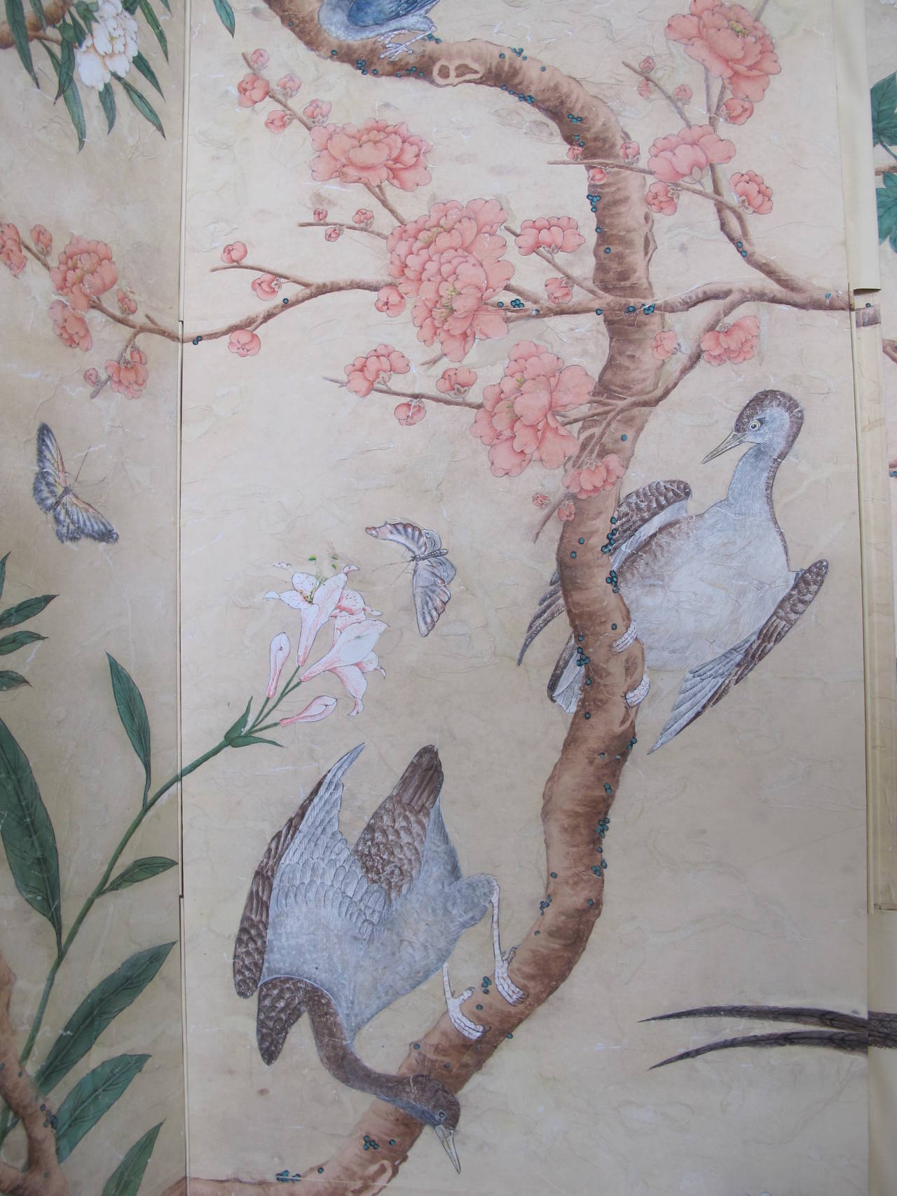 A four-panel screen with hand-painted 18th century style wallpaper applied on each panel. The design features brightly colored flowering trees, birds and butterflies. The screen has been intentionally antiqued to create the patina of an antique