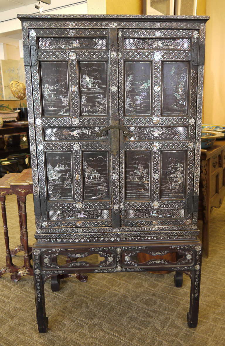 A beautifully lacquered and decorated double door cabinet on stand, inlaid with mother of pearl. 

Design is inside doors, also.

Cabinet sits upon base.