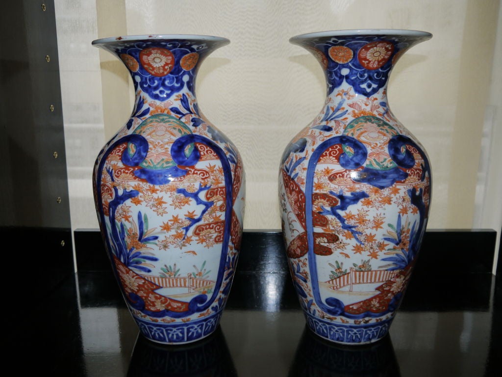 A large pair of Japanese Imari vases, with vibrant cobalt blue, orange and turquoise. With design om reserves of fence, water and

flowers.