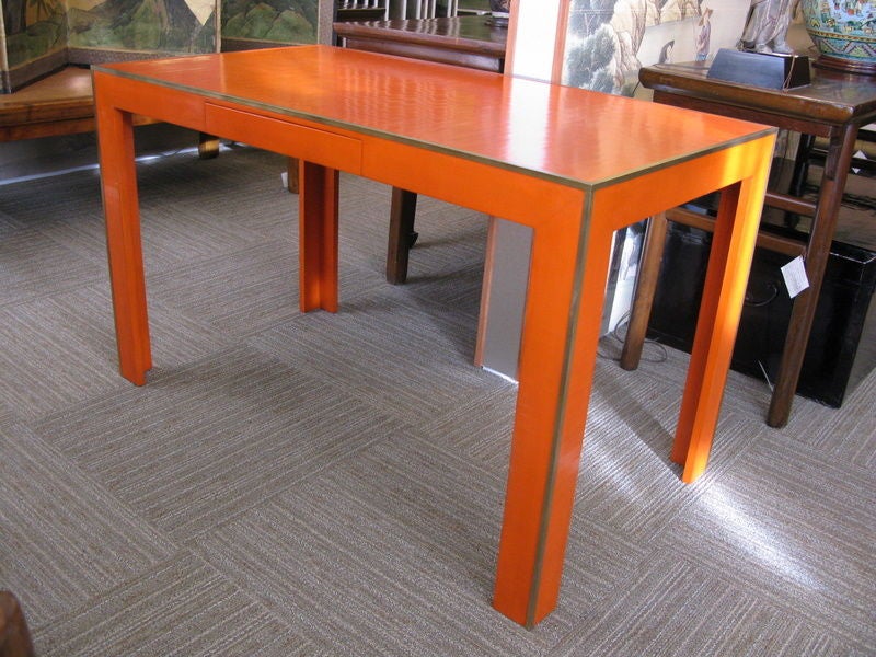 A vibrant orange lacquer desk, with crackled cashew lacquer finish, drawer in apron, straight legs, and metal edges.

Made in Gracie's studio in New York, this desk is made to order. Any color and different styles may be made to order.