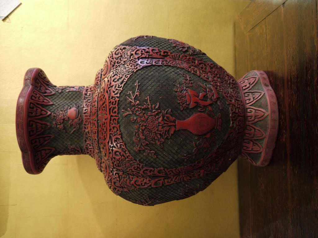 A large and beautiful Chinese red lacquer cinnabar vase with beautifully carved detail.

The vase has panels of design featuring vases with flowers, and borders with geometric designs.