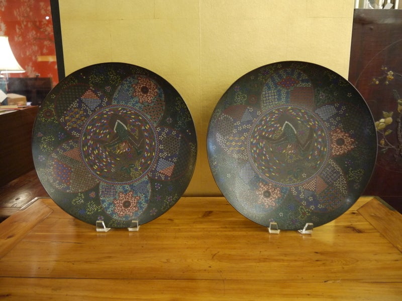 A large pair of chargers with fine detail.  Each with a large bird in the center, and floral and geometric borders in petal pattern around the center.