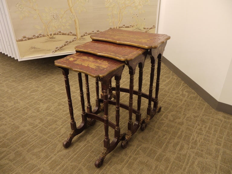 A set of three red lacquer chinoiserie nesting tables with gold landscape design, and decorative feet.

Size of largest of the three is listed.