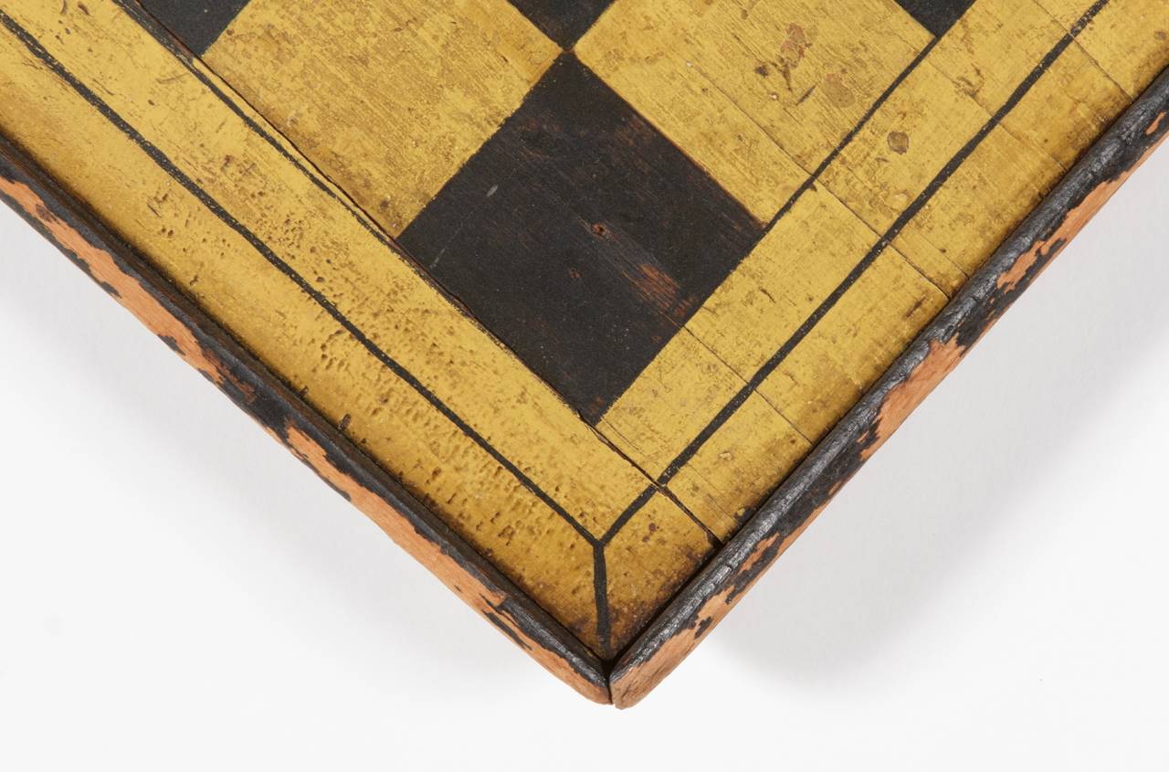 PAINT-DECORATED GAME BOARD IN CHROME YELLOW AND BLACK, AMERICAN, CA 1840-80: 

Checker or chess game board, painted in chrome yellow and black; a wonderful, early example made from a single board and with molded edges applied with cut nails.