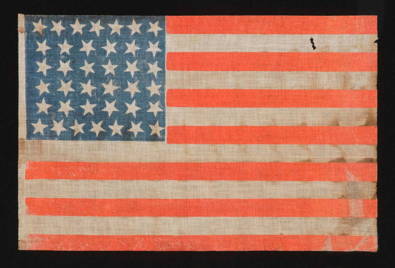 38 STARS, COLORADO STATEHOOD, 1876-1889, WITH SCATTERED STAR POSITIONING AND BRILLIANT SUNFIRE RED STRIPES:

38 star American national parade flag, printed on coarse, glazed cotton. The stars are arranged in lineal rows of 7-6-6-6-6-7 and are