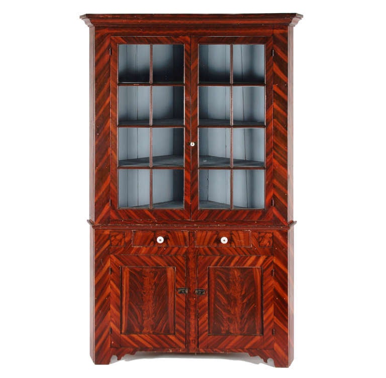 Pennsylvania corner cupboard with two, glazed, eight-pane doors over two drawers and two paneled doors below. Made ca 1840-50, the paint-decorated surface in reds and browns is a stylized representation of fancy-grained mahogany, but with an