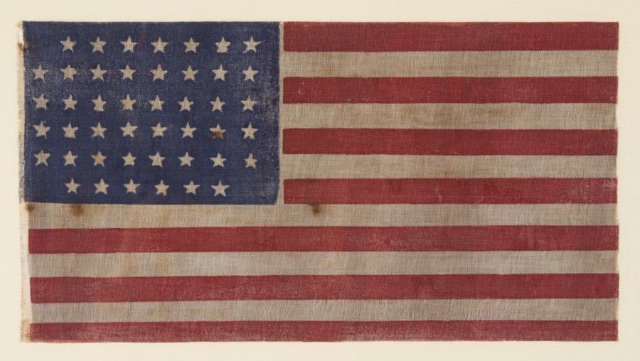 45 STARS, 1896-1907, UTAH STATEHOOD, A SCARCE, ELONGATED VARIETY WITH A RECTILINEAL STAR PATTERN THAT IS NOTCHED IN THREE CORNERS:<br />
<br />
45 star American parade flag, printed on coarse, glazed cotton. The stars are arranged in a notched