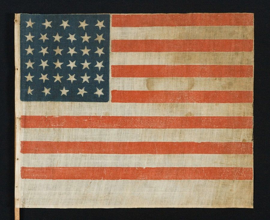 34 STARS, A CIVIL WAR PERIOD PARADE FLAG ON ITS ORIGINAL WOODEN STAFF, RARE AND WITH EXCEPTIONAL GRAPHIC QUALITIES, KANSAS STATEHOOD, 1861-63:<br />
<br />
34 star American national flag, printed on fine, glazed cotton. Note how the stars point in