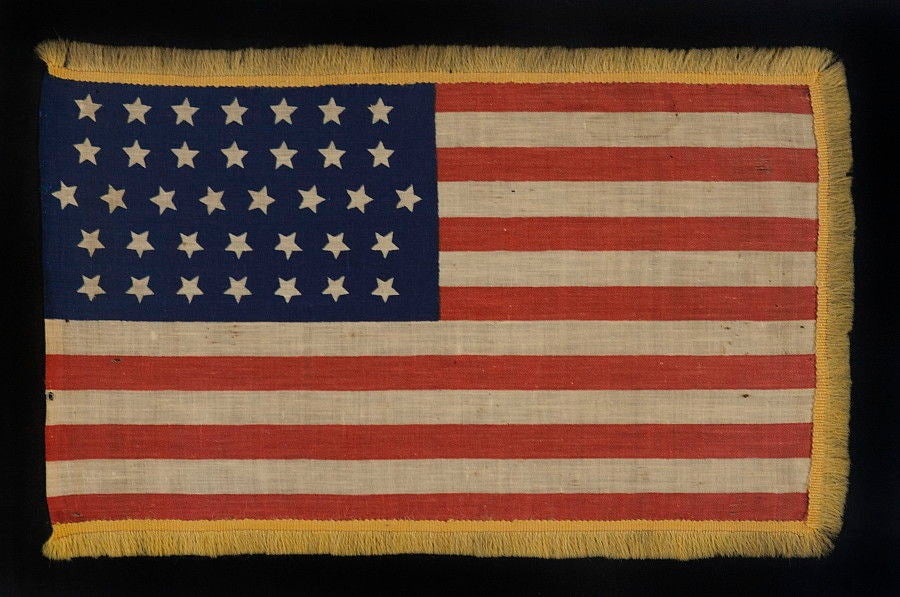 36 STARS IN A VERY ODD LINEAL CONFIGURATION FOR THIS STAR COUNT AND WITH GOLD WOOLEN FRINGE, CIVIL WAR ERA, NEVADA STATEHOOD, 1864-1867, THE ONLY KNOWN EXAMPLE IN THIS STYLE, POSSIBLY A UNION ARMY CAMP MARKER:<br />
<br />
36 star American