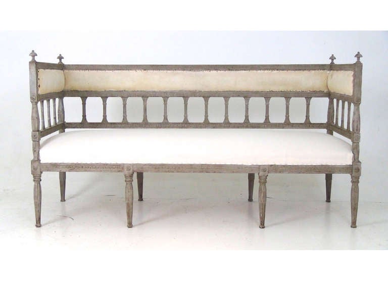 This antique sofa bench has a cream seat and back cushion with a highly detailed wood frame.