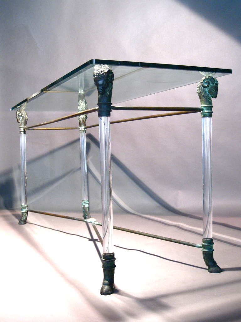 Neoclassical brass console table with lucite columned legs topped with rams heads supporting a beveled 3/4