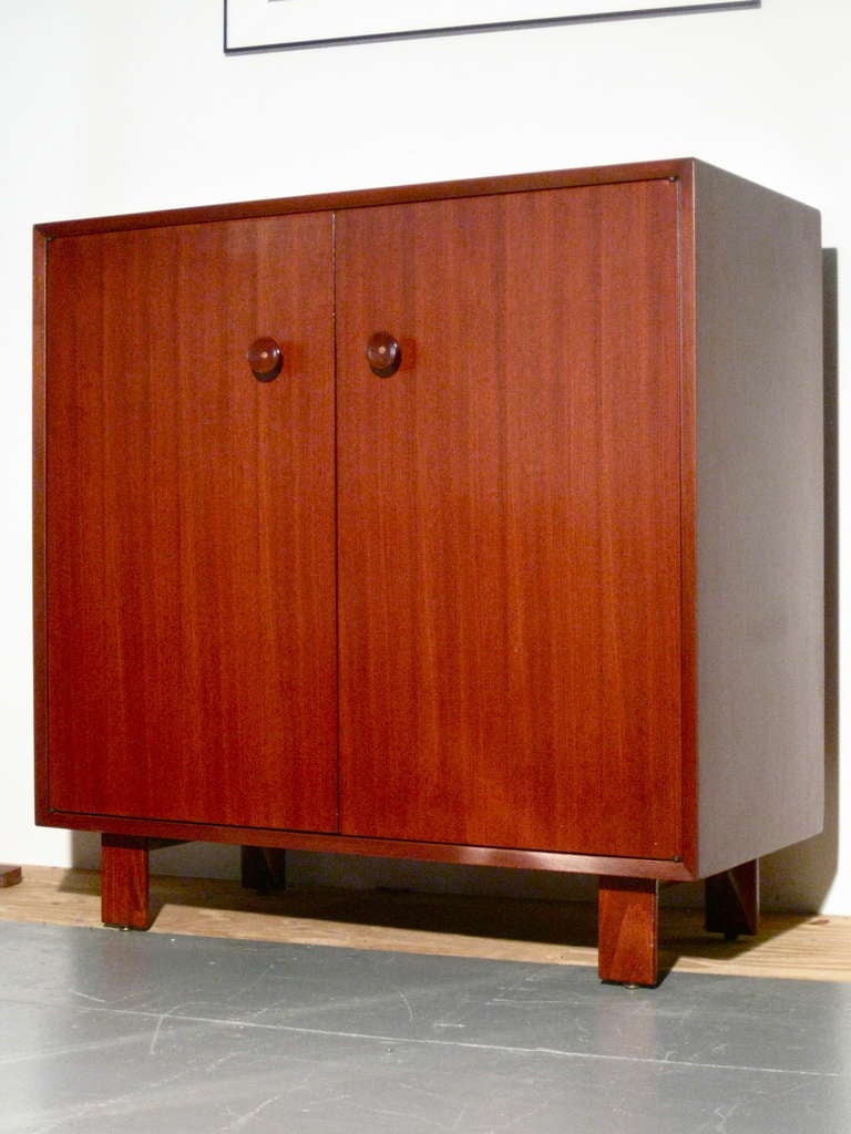 Walnut cabinet/credenza with wood & metal hardware designed by George Nelson for Herman Miller c.1950s. When opened the two cabinet doors reveal open storage on one side with two adjustable shelves and on the other side two pull out divided drawers
