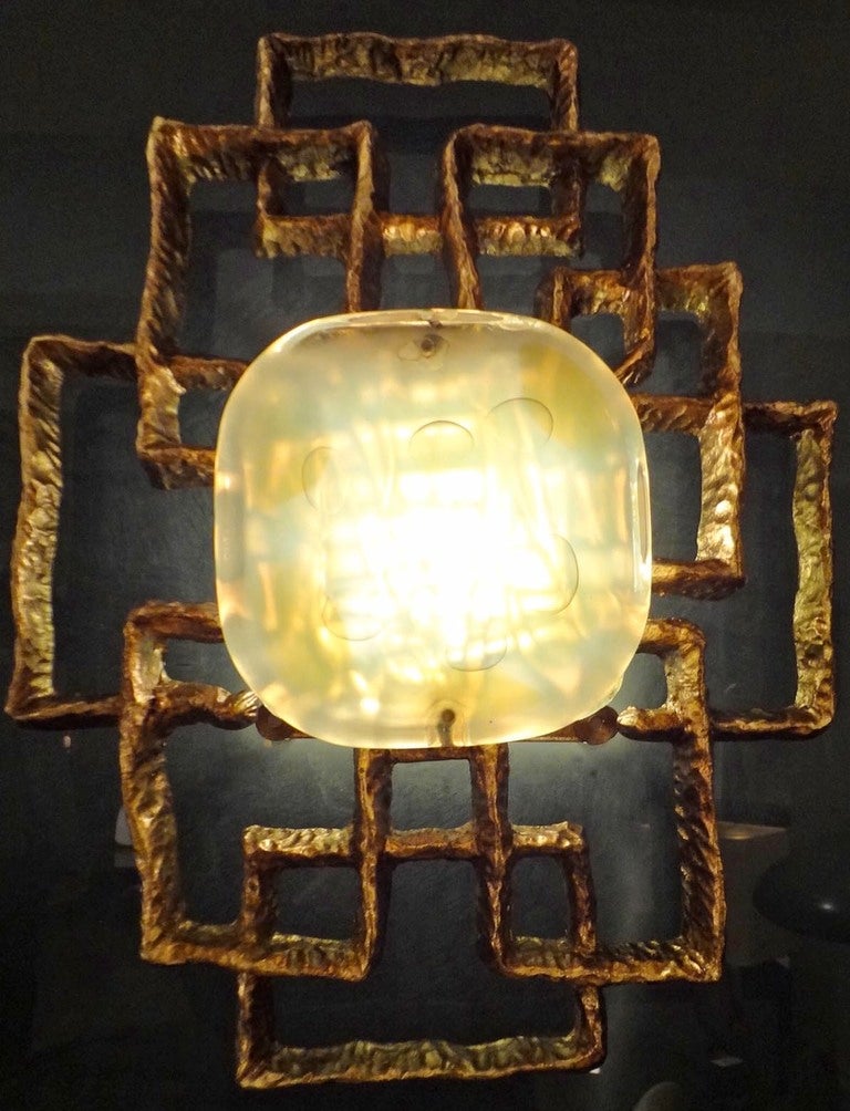 A large lit wall sculpture featuring a square smoked glass back plate that sits several inches off of the wall, onto which is attached in the center of the panel a cast bronze modernist sculpture with a large hand made piece of square opaque multi