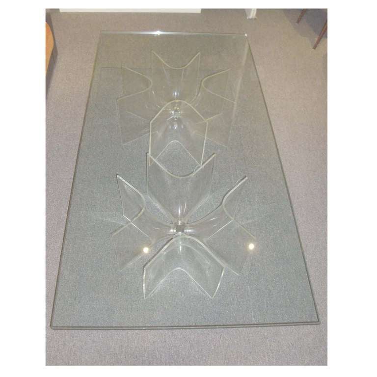 A large rectangular cocktail table featuring two pedestal bases each composed of four flower shaped plexi glass supports held together with a small steel fastener. Both bases support a large glass top. Unknown, France circa 1970.