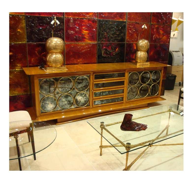 A rare sideboard featuring a modernist shaped body in Lemonwood on a plinth base with convex shaped foot, two doors with shelf interiors and four central drawers with antiqued mirrored fronts with applied decorative gilt brass circles on the doors.