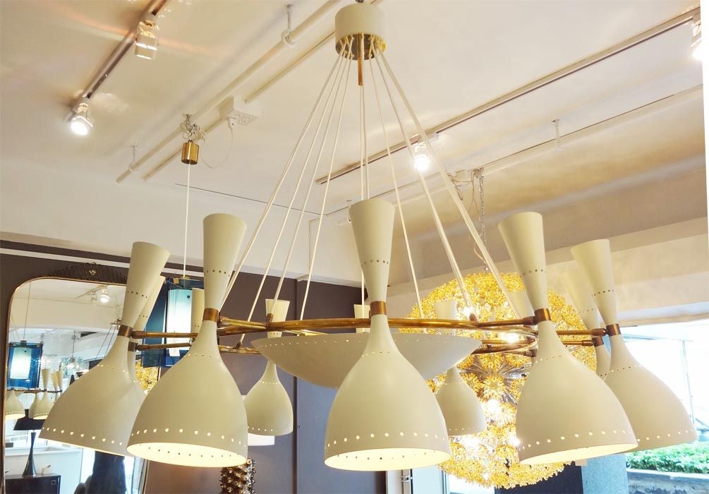 A large scale twelve light mid century chandelier featuring a frame in brass with twelve white wire hanging supports, twelve perforated adjustable cone shaped light diffusing shades in off white lacquered metal and an interior perforated bowl with