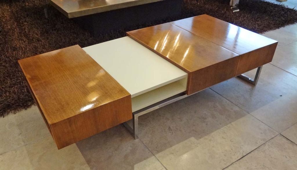 A Modernist cocktail table featuring a frame in chromed steel which supports a sectioned top in off white lacquer and Mahogany. The two end Mahogany sections side towards the center creating the size table needed. When the sections are fully