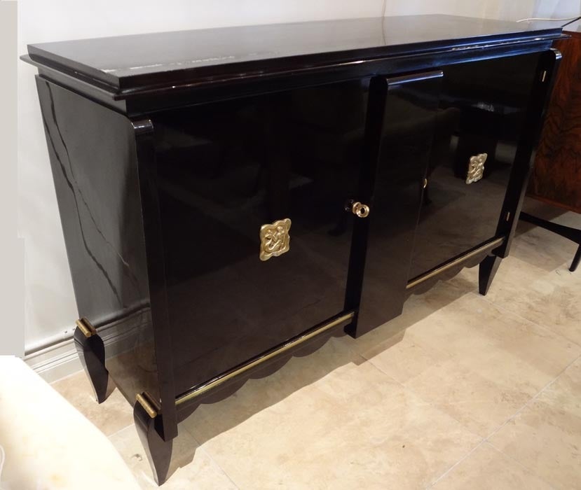 An Art Deco sideboard featuring a body in deep brown stain with two front doors, a scrolling front skirt, shaped tapering legs, a banding in gilt brass and two central door decorations featuring stylized mermaids. In the style of Andre Arbus, France