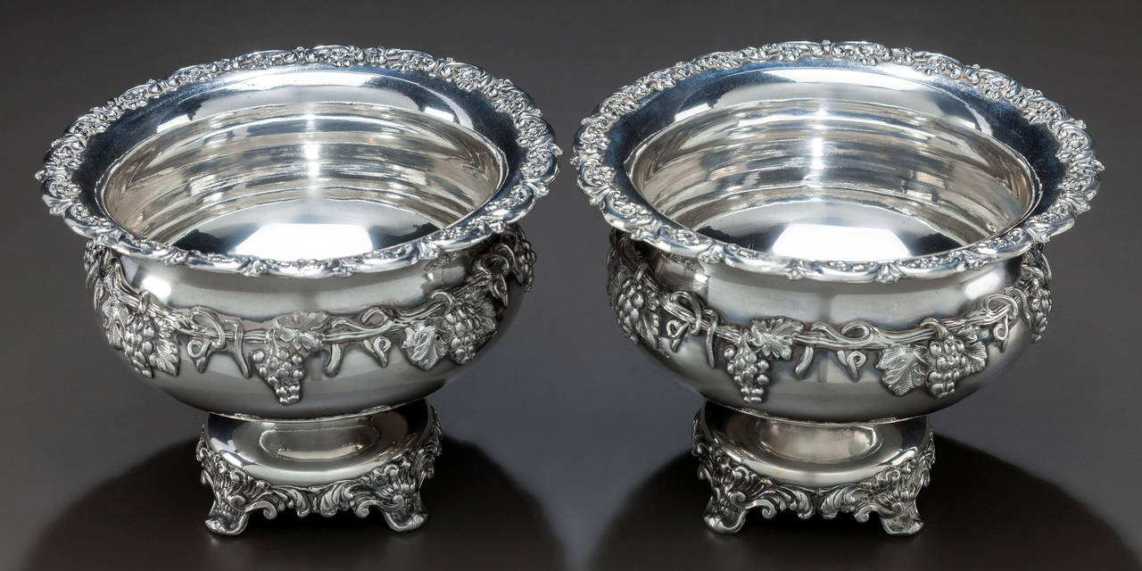 A pair of early 20th century French silver plated compotes with cast rims of C-scrolls and flowers over waisted neck, body encircled with grape and vine motif, raised on squat stem continuing to spreading circular foot, further set on four cast