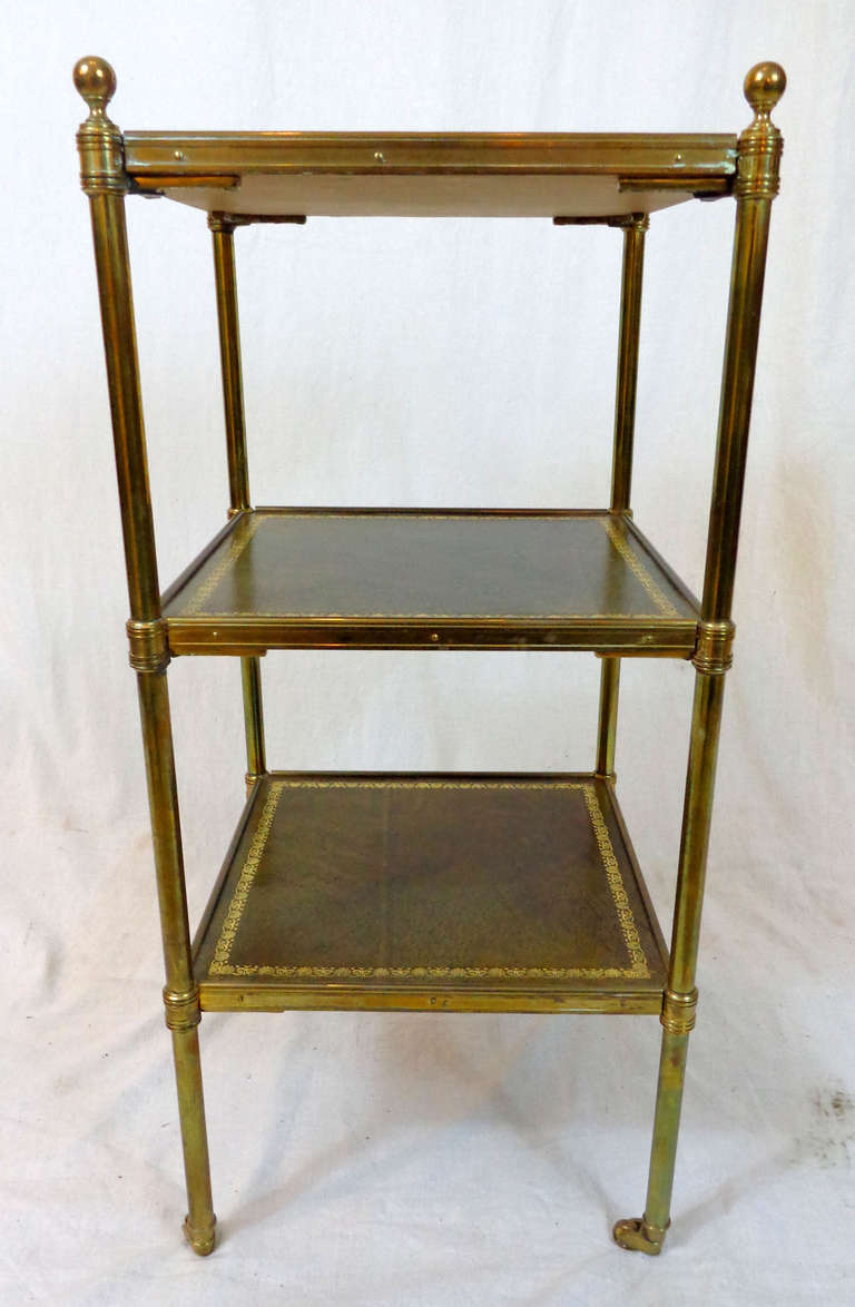 Mid-century English three-tiered rolling side table with embossed leather surfaces and brass supports, finials, and casters.