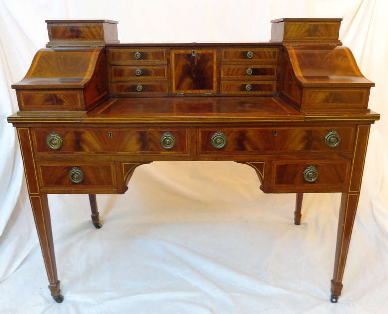 Unique Carlton House Style Desk with sliding writing surface, secret compartments, and a letter slot.  The desk has its original flame mahogany finish and note handsome banding and stringing.  With original brass casters and drawer pulls.