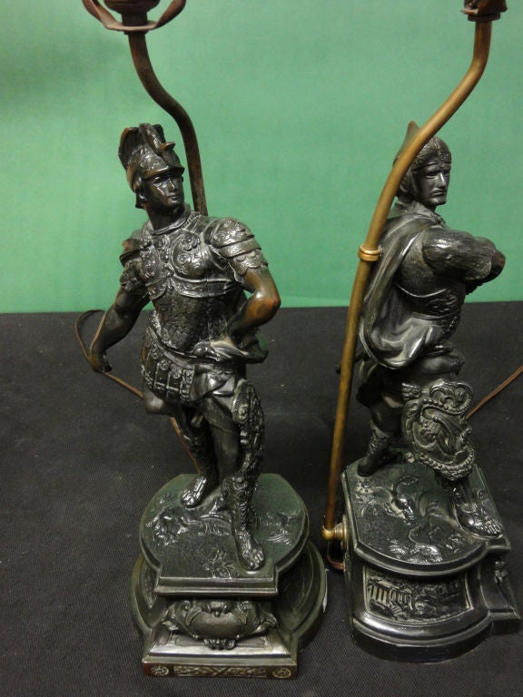 A Pair of Late 19th Century Sculptures Depicting Roman Soldiers now as Lamps. Sculpted with wonderful attention to detail - note Coliseum carved on the sides & each soldier  displays a unique shield. Most likely these were probably part of a clock